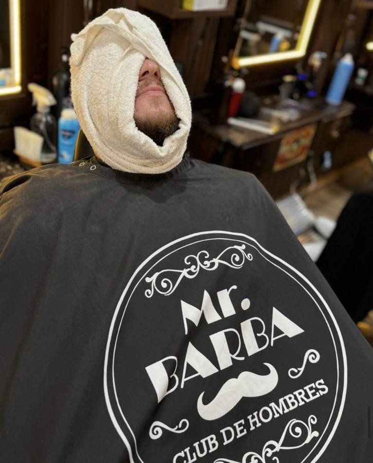 Cliente con toalla caliente en la cara durante el ritual de barba